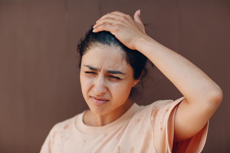 A woman wearing an orange shirt is sweating and holding her head. 