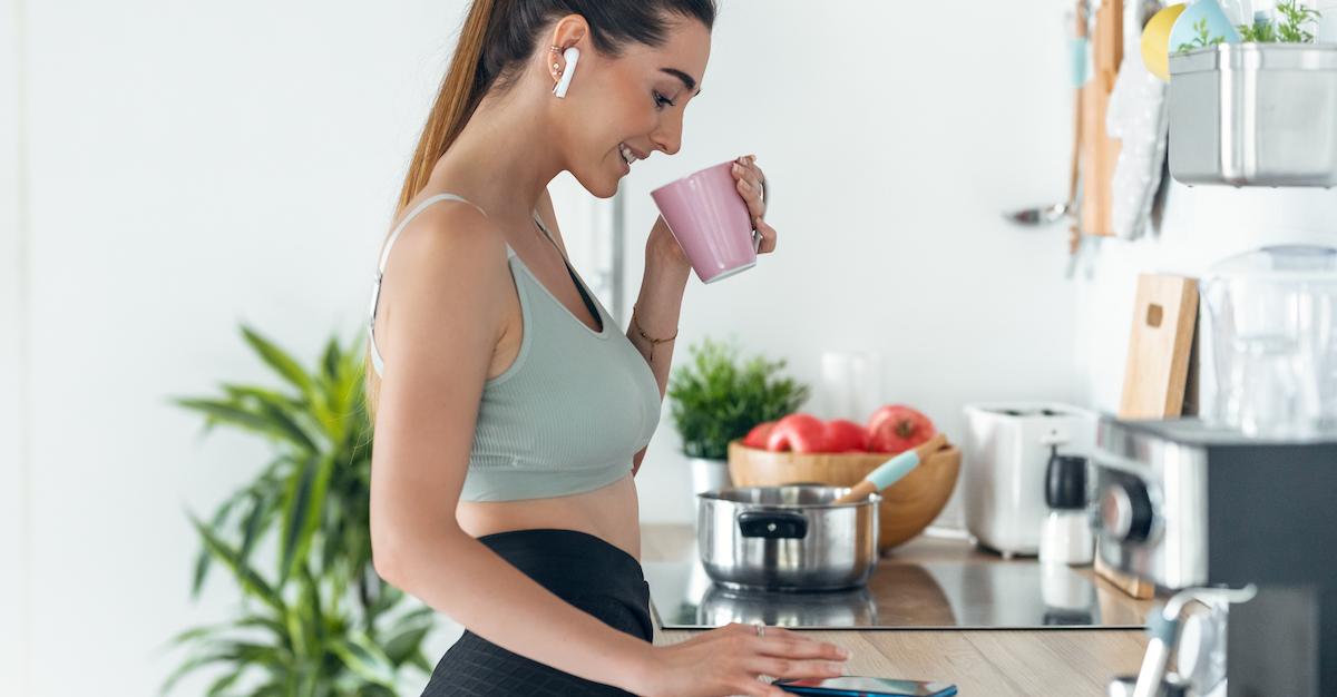 A woman wearing workout clothes drinking coffee while checking her phone.