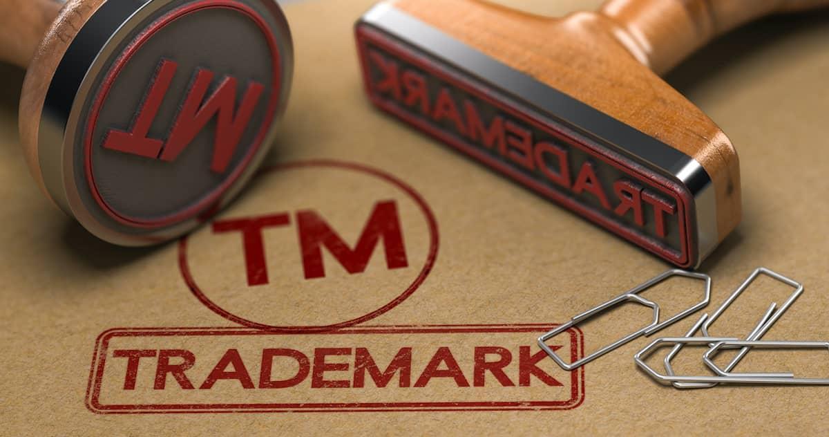 Two rubber stamps: one with trademark and one with TM, lying next to some paper clips:  