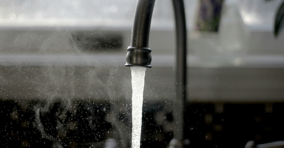 Water streams out of a kitchen faucet, leaving moisture droplets in its wake