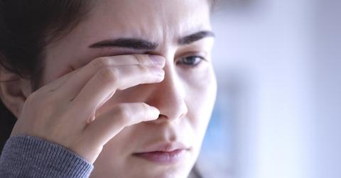 A woman puts her hands to her eye with a concerned look.