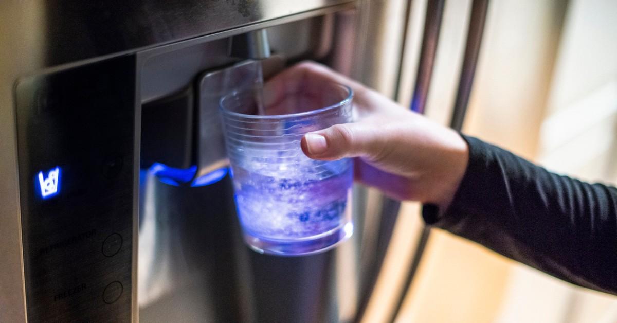 A person fills up their water glass from their fridge door