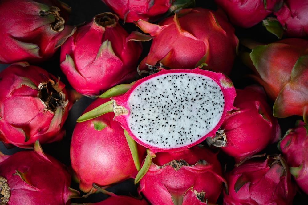 A dragon fruit cut in half on top of of whole dragon fruits. 