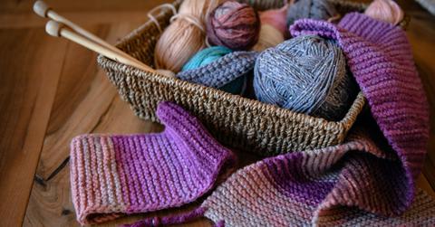 A woven basket full of yarn and knitting needles on a table.
