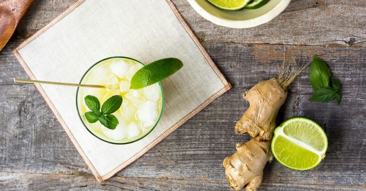 A cup of ginger beer sits on a napkin, surrounded by linden, mint and ginger roots