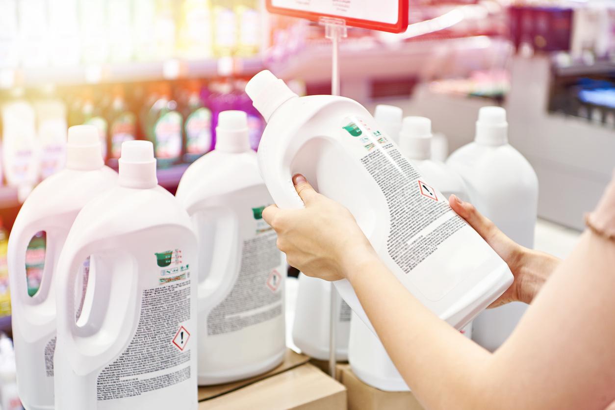 A person reads the safety label on the back of a white bottle of bleach in a grocery store aisle.