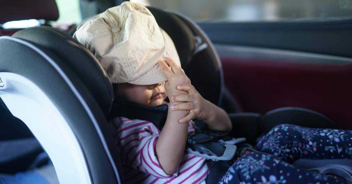 A child pulls her hat down over her eyes while sitting in a car seat