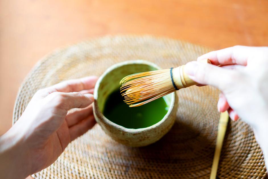 A person mixes matcha in a bowl with a whisk.