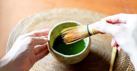 A person mixes matcha in a bowl with a whisk.