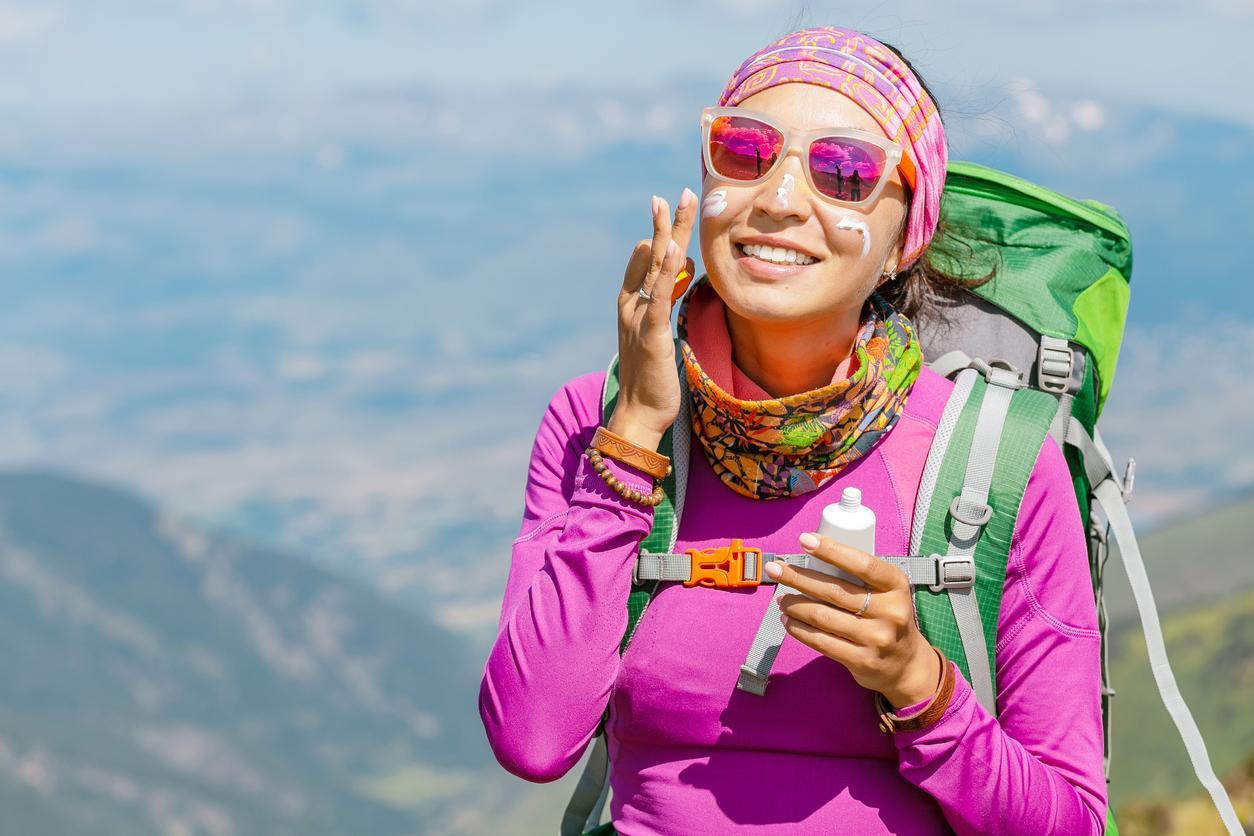 Person wearing a long sleeve and carrying a backpack putting sunscreen on while hiking.