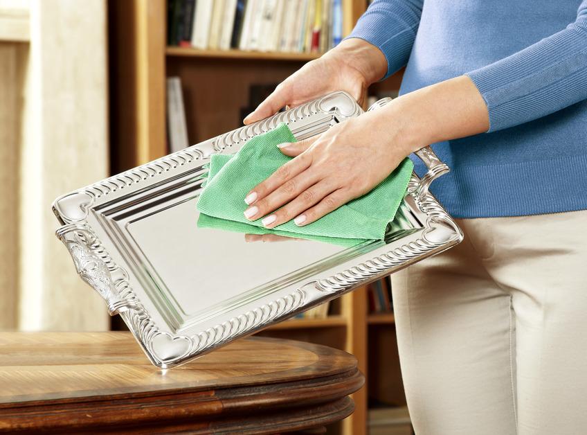 A woman using a green clothing to clean a shiny metal tray.