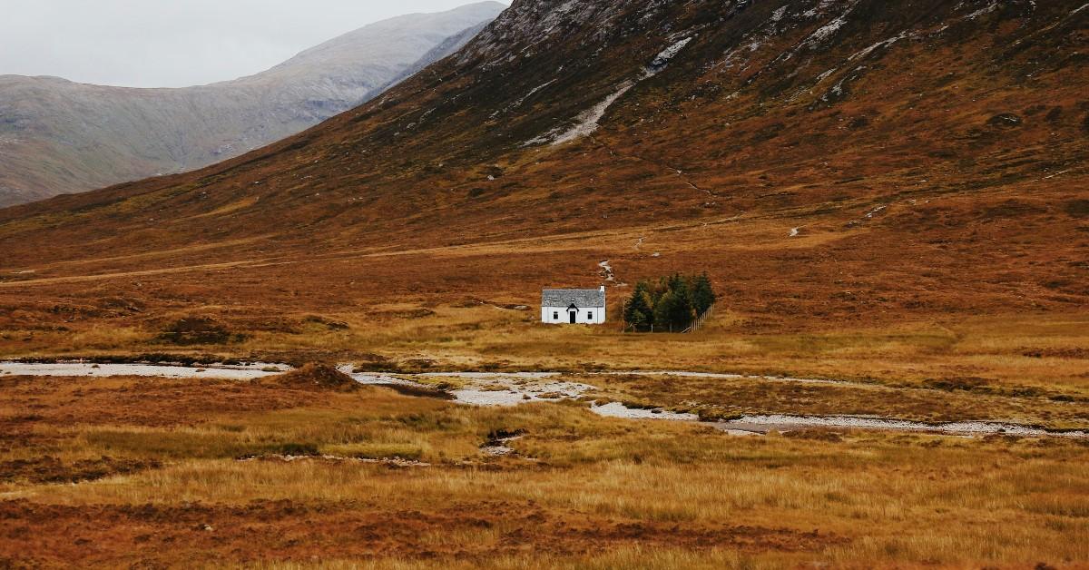 A white house sits in the middle of an wide expanse of nothingness at the bottom of a mountain range