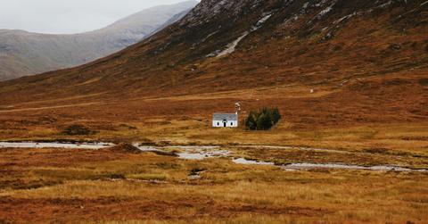 A white house sits in the middle of an wide expanse of nothingness at the bottom of a mountain range