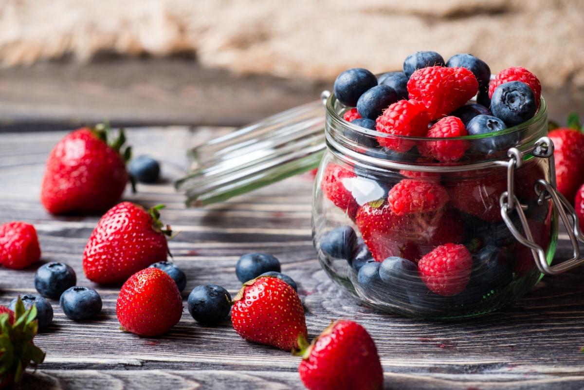 Strawberries, blueberries, and raspberries in glass jar and on table