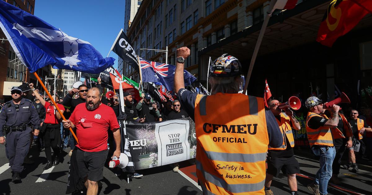 Laborers in Australia protest during a May Day march with signs, flags, and fists raised.