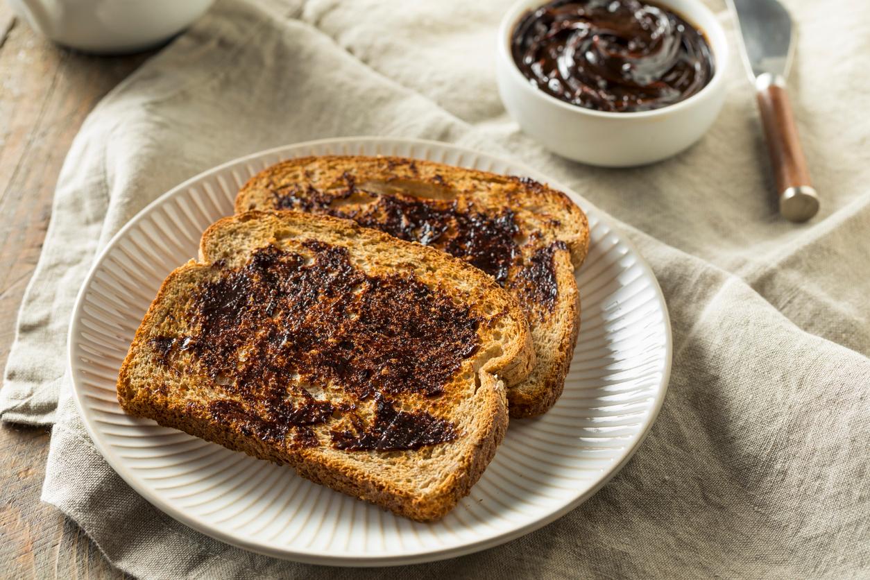 Two pieces of toast with Vegemite spread on top are featured atop a plate on a gray napkin.