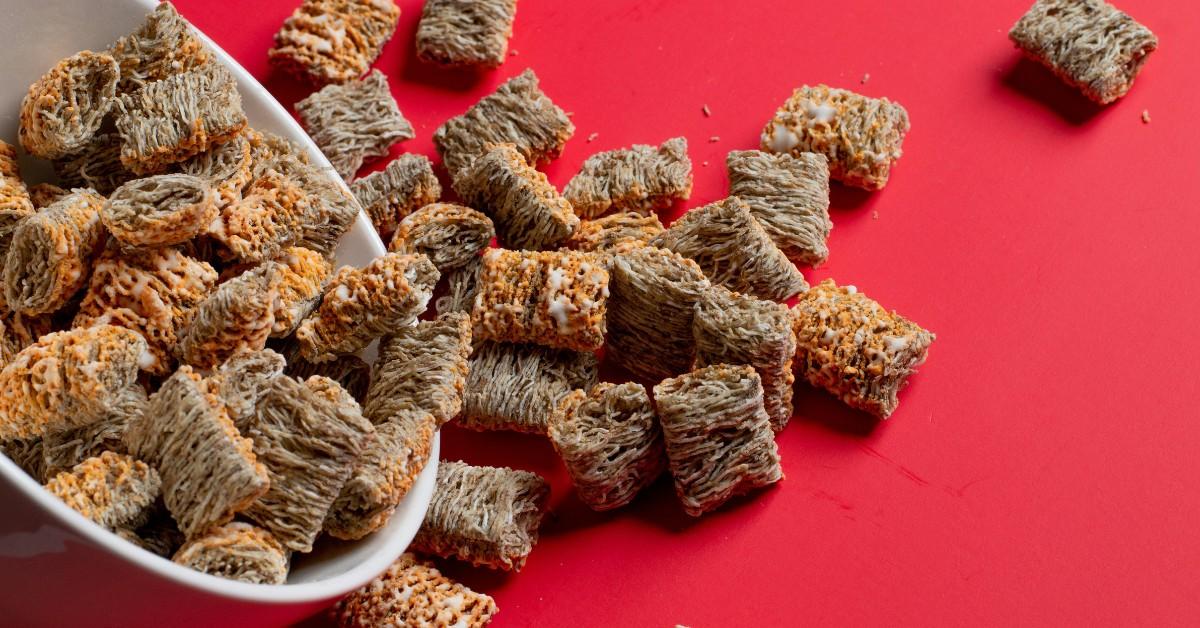 A bowl of shredded wheat style cereal sits half spilled on a red background 