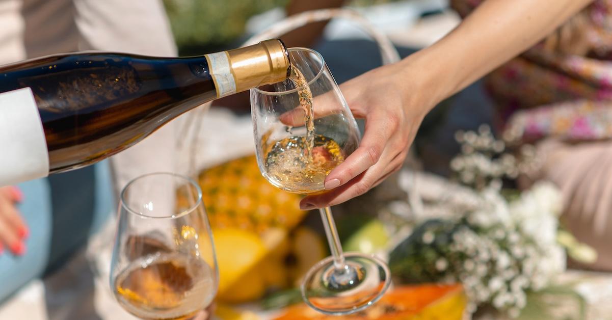 Bottle of white wine poured into glass in front of a picnic setup