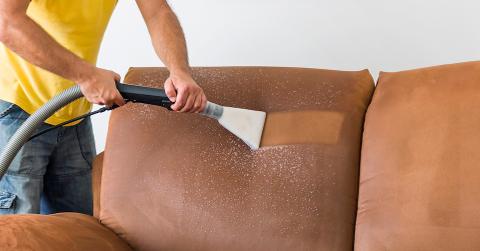 A person uses a vacuum to clean a brown fabric couch.