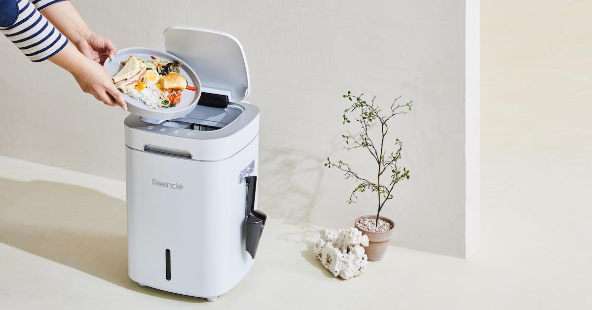 A pair of hands holds a plate of food over a white Reencle machine.