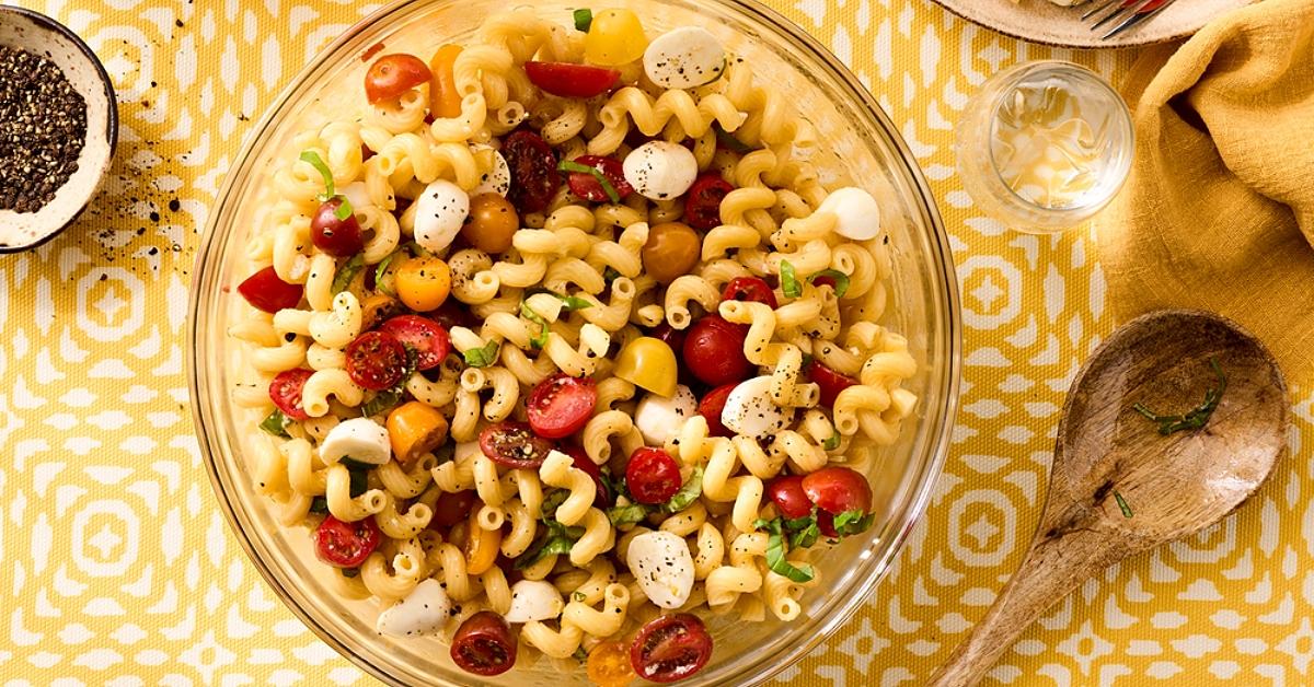 Overhead photo of a bowl of pasta salad made with Barilla Protein+ Cellentani on a yellow patterned table cloth