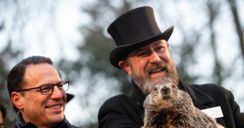 The groundhog named Punxsutawney Phil is handled by two men in coats beside a crowd of more than 5,000 people in the winter.