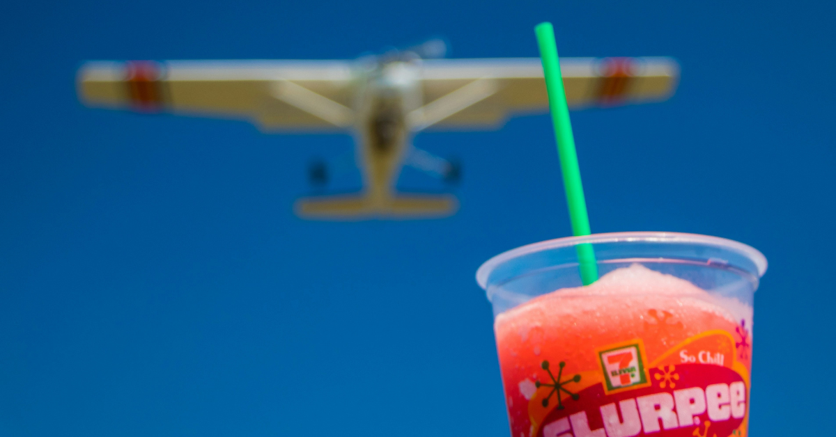 A Slurpee is held up to the sky as a plane flies in the background