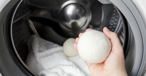 Hand holds a white dryer ball in front of a dryer