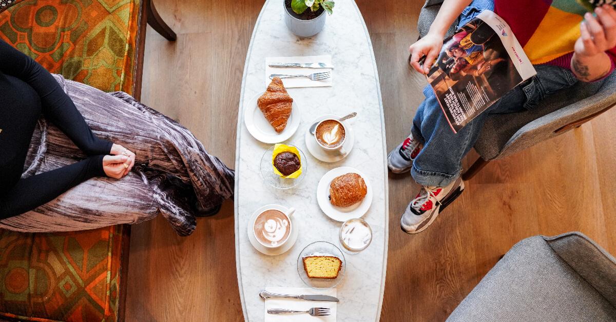 Overhead photo of two people sitting at a table covered in pastries and mugs of coffee in Purple Waves café 