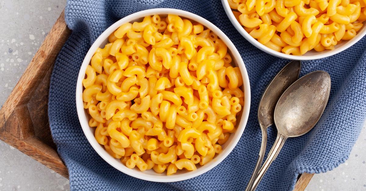 Bowl of mac and cheese on a blue blanket served in a wooden tray. 