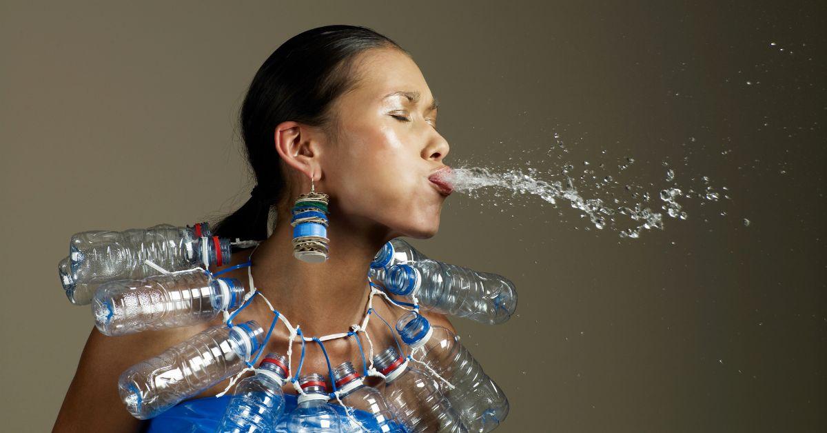 Woman wearing a recycled water bottle necklace and spitting out water.