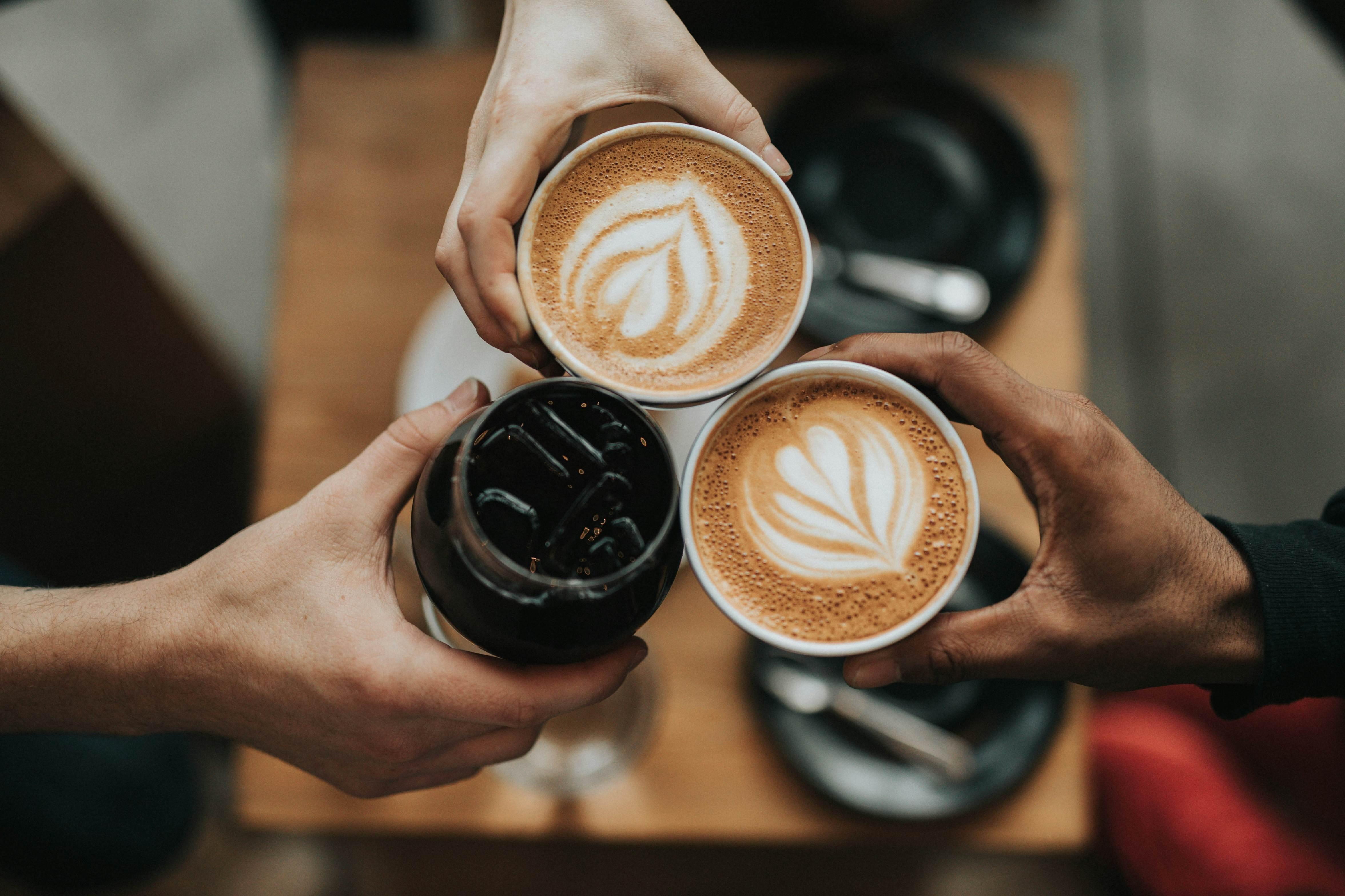 Three people hold up their coffee drinks, pictured from above.