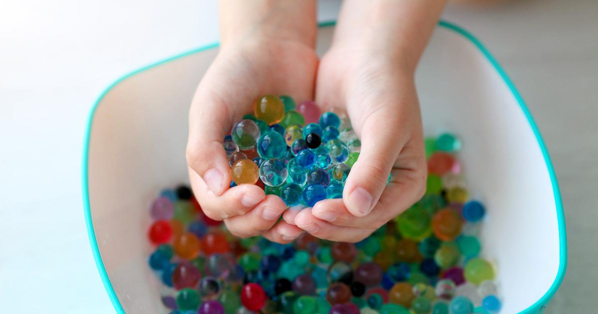 Child's hands hold water beads over bowl