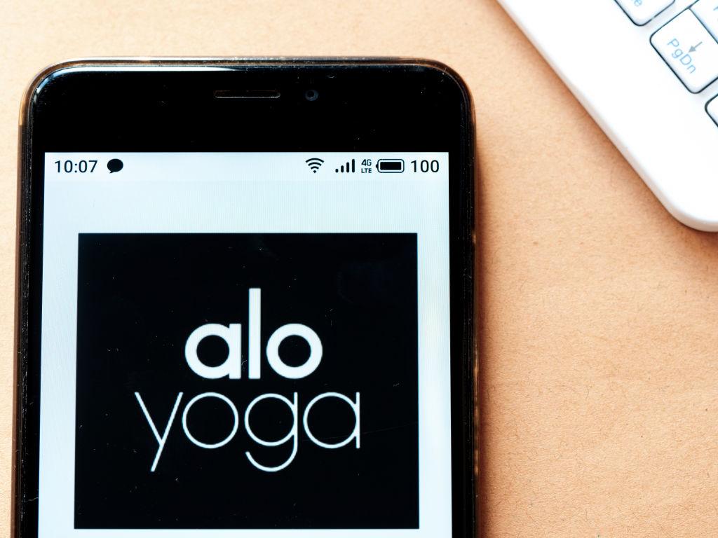 A cellphone depicting the words "alo" and the word "yoga" against a peach-colored background.