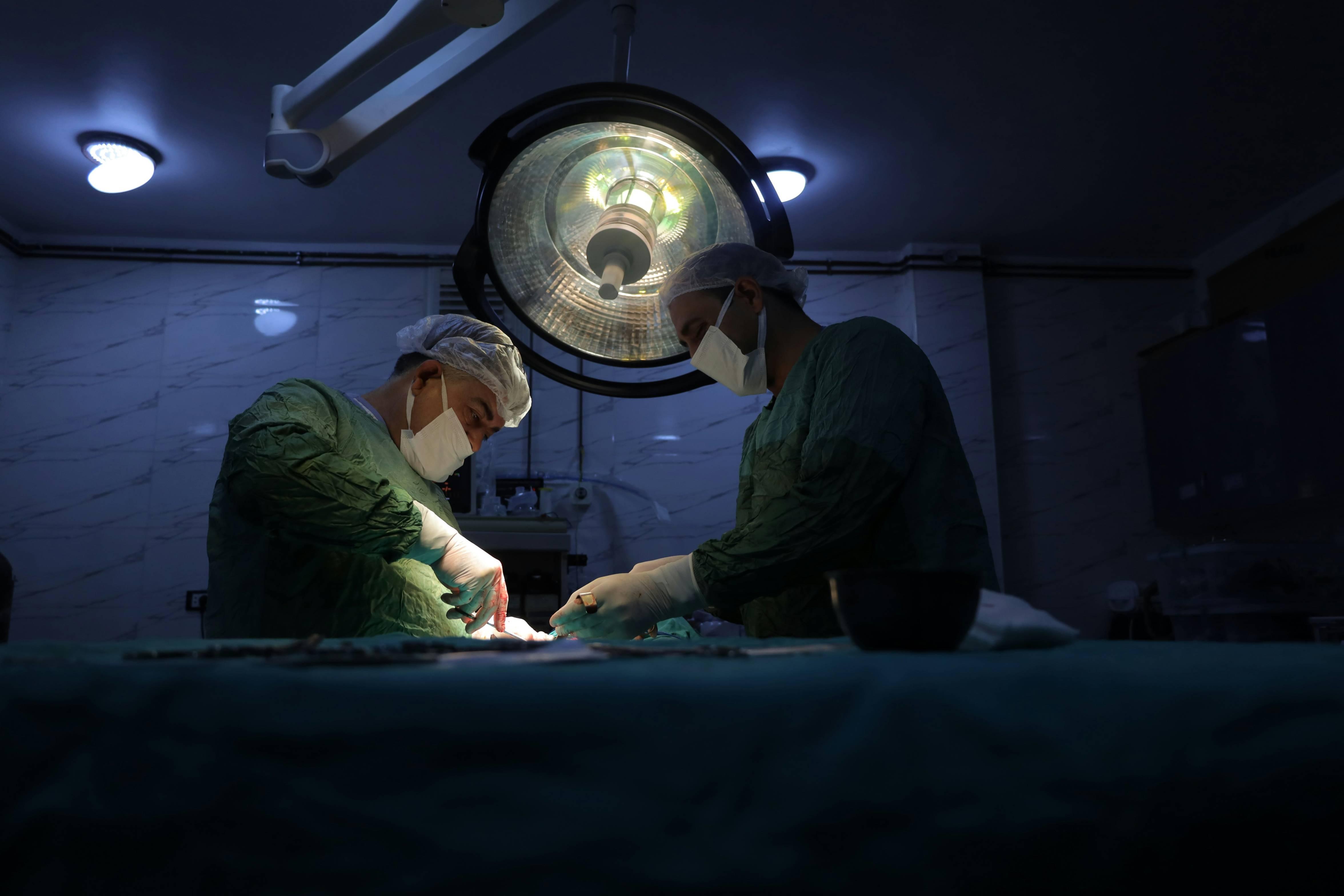 Two masked surgeons operate on a patient.