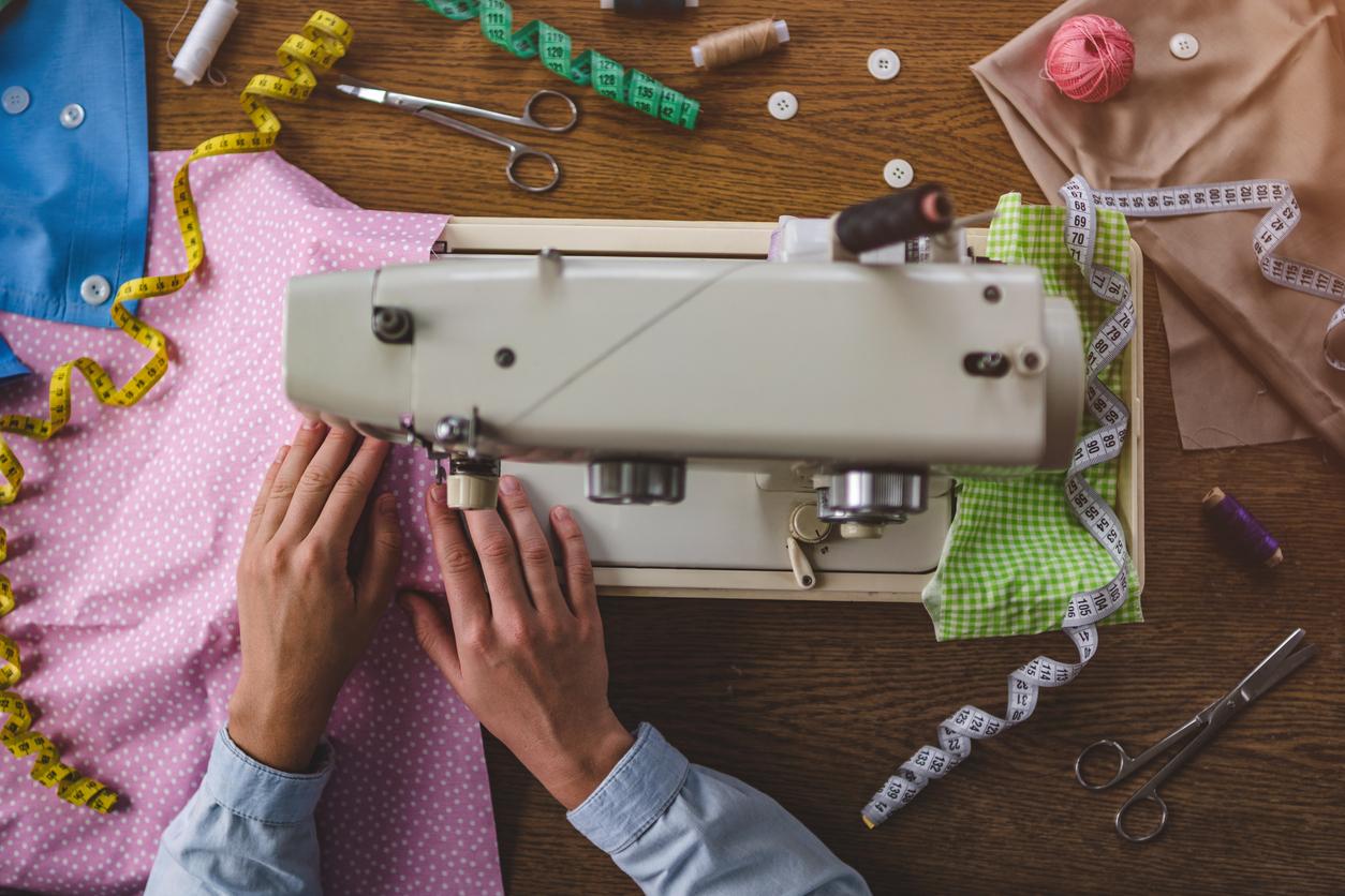 Overhead view of someone using a sewing machine on a wood table with various sewing supplies around it.