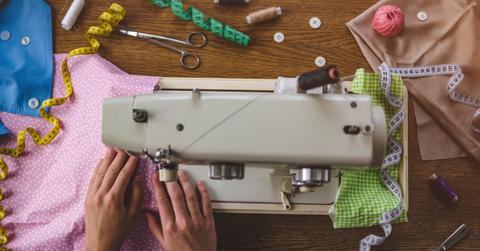 Overhead view of someone using a sewing machine on a wood table with various sewing supplies around it.