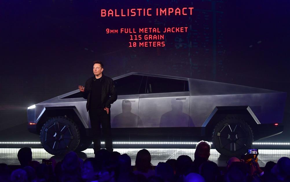 Elon Musk stands in front of a Tesla Cybertruck at a demonstration in front of a crowd. 