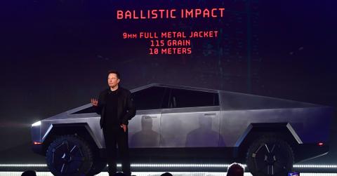 Elon Musk stands in front of a Tesla Cybertruck at a demonstration in front of a crowd.
