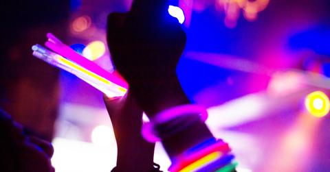 A person at a rave wears multiple glow sticks around their wrist while holding glow sticks in their other hand.
