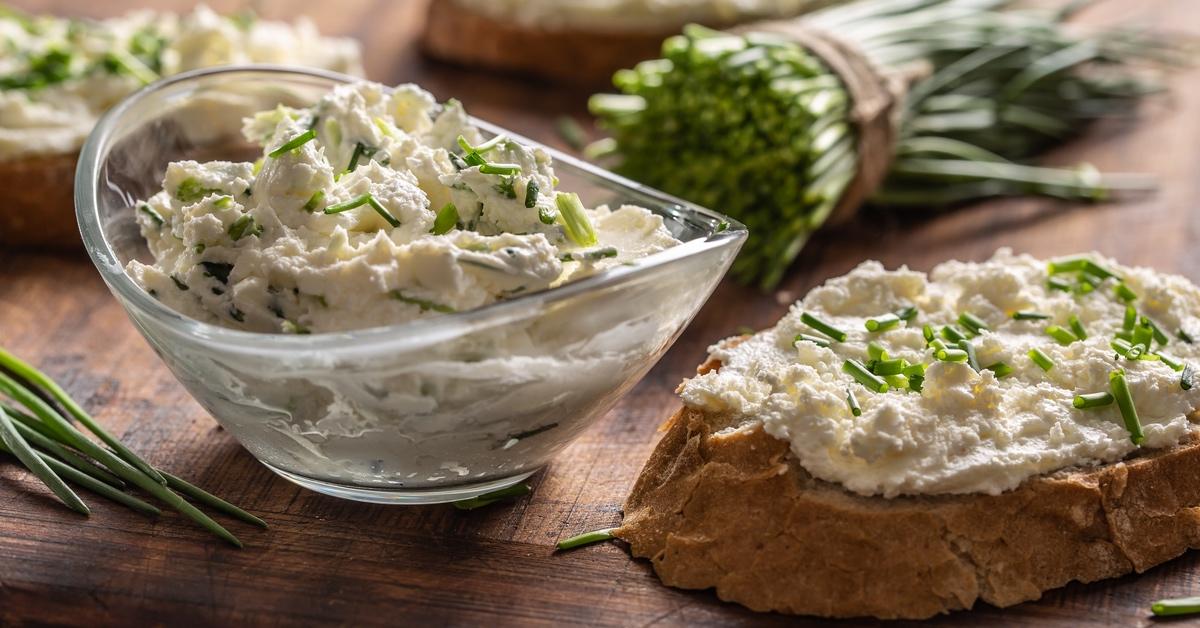 Cream cheese with chives in a bowl and on a slice of bread.