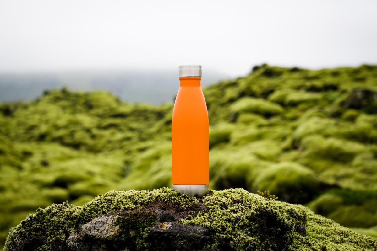 orange metal water bottle outside on a mossy rock