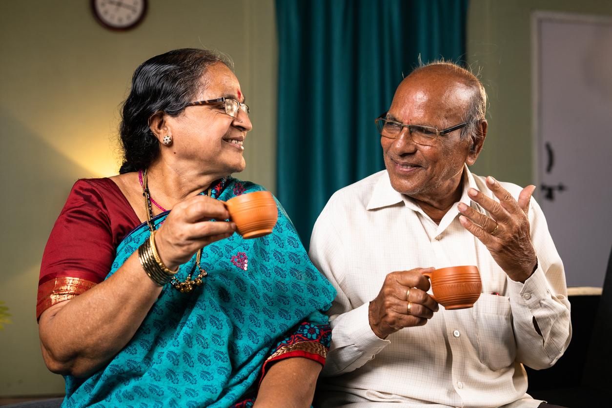 A married couple from India drink chai tea from matching orange cups as they smile at one another.