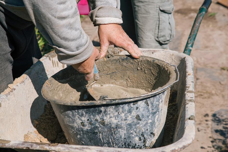 Stock photo of person kneading cement in a bucket. 