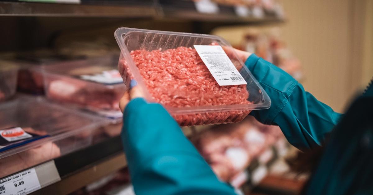 Woman holding ground beef in packaging at a supermarket.