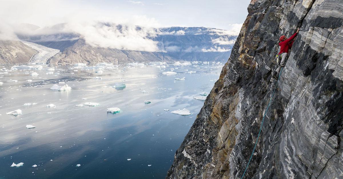 Alex Honnold climbing Ingmikortilaq mountain, with icy water and mountains in background.