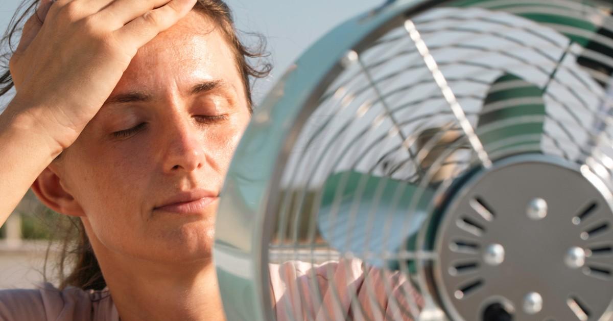 A woman gets close to a large fan to try and cool down on a hot day