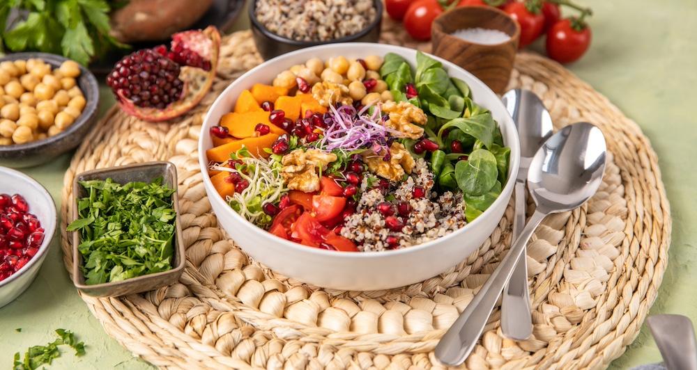 A colorful salad in a white bowl on a woven placemat.