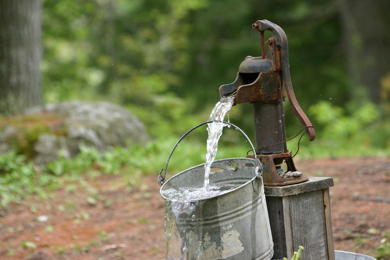 Water coming out of an antique water pump and flowing into a bucket.