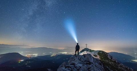A person on a mountain pointing a torch light towards the space. (Representative Cover Image Source: Pixabay | Felix Merler)